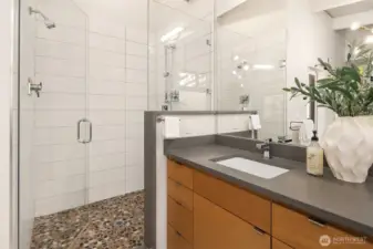 The spa bathroom includes both shower and soaking tub. This stone flooring is reminiscent of the aggregate main entry way and the local coastal overall flavors.