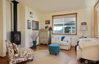 Cozy living room with fireplace, fantastic window package for light (sellers have installed shades for privacy) and pretty hardwood flooring in the great room space and hall leading to Primary Suite, Office and Half Bath.