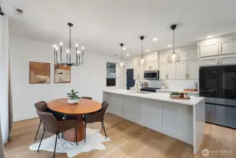 Bright entertainer’s kitchen featuring a large island with seating, modern lighting, and extensive cabinetry extending along the wall for added storage and functionality. The layout is designed for both daily living and gathering with friends and family.