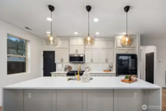 Clean-lined kitchen design centered around a large island and full wall of cabinetry, offering abundant storage and prep space. Pendant lighting and recessed ceiling lights keep the kitchen bright and welcoming throughout the day.