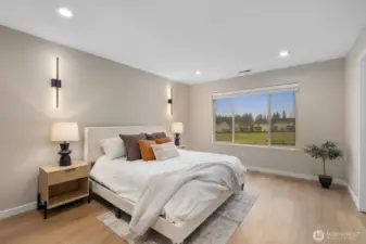 Spacious primary bedroom filled with natural light from a large picture window overlooking the open green space beyond the home. The generous layout allows for comfortable furniture placement, creating a peaceful and relaxing retreat.