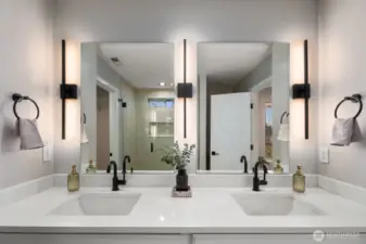Bright primary bathroom featuring a wide dual vanity with two sinks, large mirrors, and modern wall lighting that evenly illuminates the space. The clean design and spacious counter area create a functional and comfortable daily routine space.
