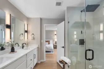 Primary bathroom showcasing a spacious glass-enclosed walk-in shower and expansive vanity area. The open layout connects seamlessly back to the primary bedroom, creating a private and well-designed primary suite experience.