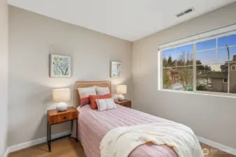 Light-filled bedroom with large window bringing in neighborhood views and natural daylight. A comfortable layout with space for bedside tables creates a calm and functional retreat within the home.