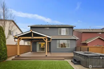 Rear exterior of the home showcasing the covered deck structure and expansive outdoor entertaining area. The backyard features clean landscaping and a dedicated space for the hot tub.