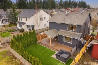 Aerial view showcasing the fully fenced backyard, covered outdoor deck, and surrounding neighborhood setting. The layout highlights the private yard space and outdoor living area directly behind the home.