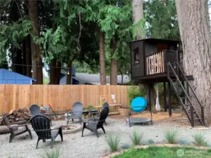 The backyard boasts a charming treehouse, a cozy fire pit area, and beautiful old-growth trees. There's also a spacious grassy area that, with a little love, could become the perfect outdoor retreat. (Shown in summer)