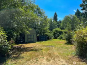 Entrance to the lot from W Cedar. Nice open space with beautiful greenery surrounding the property. Fruits, berries and shade trees (with a babbling brook along the east lot line.) Like your own Garden of Eden! Great storage structures. Room to keep your boat and RV!