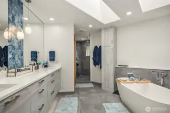 A lavish, stunning, 5-piece en suite bath boasting heated floors, soaking tub, floating dual vanity, large pass-through shower with rain head, bench, and beautiful tilework, fixtures & lighting.
