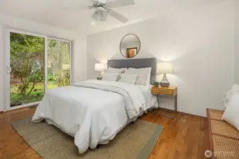 Serene primary bedroom with hardwood floors and direct access to the backyard, offering a peaceful retreat surrounded by greenery.