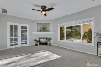 The family room, with its gas fireplace and a wall niche. The room also has a ceiling fan incorporating an overhead light. French doors lead to an office. There are large windows overlooking the backyard's continuously flowing fishpond.