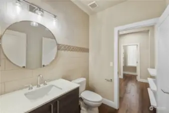 The main level powder room offers a glass tile wall, floating vanity with quartz and conveniently flows to the mudroom and wraps to the kitchen