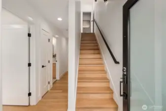 A welcoming foyer leads past main-floor bedrooms and bath, with warm wood floors and a clean modern staircase drawing you up to the open-concept living and kitchen spaces above.