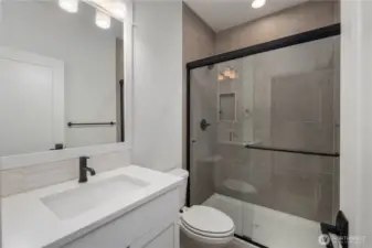 Main-Level Guest Bathroom:  This well-appointed bath features a wide quartz-topped vanity, soft neutral tilework, and a frameless glass shower enclosure accented with matte black hardware. Its thoughtful layout supports comfort and convenience for guests or main-level living. With Gooden Hollow’s Bothell location in the Canyon Park corridor, this space benefits from close proximity to parks, everyday amenities, and major commuter routes. Clean lines and modern fixtures bring a polished, cohesive feel to this main-floor bath.    These photos are from Lot 5 at Gooden Hollow, the home listed here. However, other homes in the community will have changes, so all photos, renderings, site maps, and floorplans are for visualization purposes only. Plans, colors, building orientation, finishes, home outlook, and other details can and WILL vary.