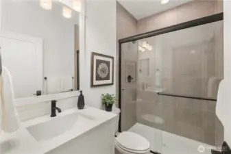 Main-Level Guest Bathroom:  This well-appointed bath features a wide quartz-topped vanity, soft neutral tilework, and a frameless glass shower enclosure accented with matte black hardware. Its thoughtful layout supports comfort and convenience for guests or main-level living. With Gooden Hollow’s Bothell location in the Canyon Park corridor, this space benefits from close proximity to parks, everyday amenities, and major commuter routes. Clean lines and modern fixtures bring a polished, cohesive feel to this main-floor bath.    These photos are from Lot 5 at Gooden Hollow, the home listed here. However, other homes in the community will have changes, so all photos, renderings, site maps, and floorplans are for visualization purposes only. Plans, colors, building orientation, finishes, home outlook, and other details can and WILL vary.