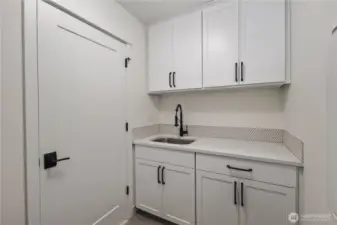 Laundry Room (Sink + Cabinetry Wall):  A secondary laundry workspace features expansive countertop space, deep utility sink, and full-height cabinetry for storing essentials. This thoughtful layout supports multitasking—folding, soaking, sorting—while keeping the rest of the home clutter-free. Positioned in Bothell’s Canyon Park neighborhood, it brings a practical rhythm to daily living near local shops, trails, and commuter routes. The stylish tile backsplash adds subtle texture and elevates the room with a polished, modern touch.    These photos are from Lot 5 at Gooden Hollow, the home listed here. However, other homes in the community will have changes, so all photos, renderings, site maps, and floorplans are for visualization purposes only. Plans, colors, building orientation, finishes, home outlook, and other details can and WILL vary.
