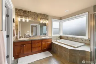 Primary ensuite highlights a generous soaking tub with tile detail and dual vanities.