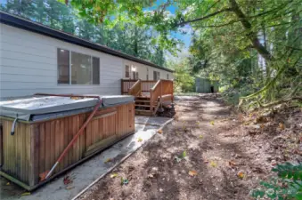 View of back of home with partially used working hot tub.  See the new back deck leading to everything you want to do outside with nature.  There is older shed in view for tools and other storage items available.  There is full exterior new white paint new roof and windows also.  Check out the large concrete pad under the hot tub also