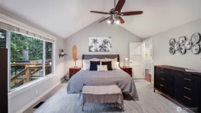 Primary suite located on the main level with vaulted ceiling, ceiling fan, walk-in closet, and en suite.