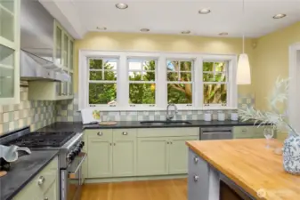 Even dish duty feels delightful with a wall of windows overlooking the home’s tranquil backyard, framed by soft green cabinetry and warm stone counters.
