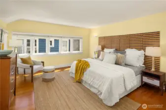 Sunny primary bedroom with warm fir floors and plenty of space for a seating area.
