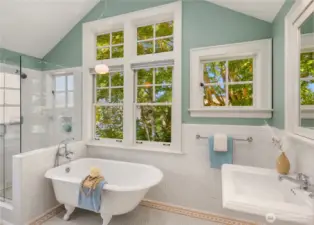 The spa-like primary bath features a clawfoot soaking tub framed by tree-filled views, separate shower, and timeless tile finishes.