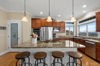Kitchen appliances include a 5 burner propane cooktop, built in double ovens, a microwave, and stainless steel refrigerator freezer and dishwasher. A walk in pantry is ahead on the left.