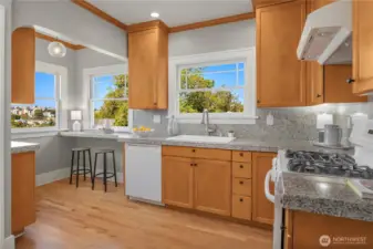 The spacious kitchen features granite counters, maple cabinetry, and a convenient breakfast bar framed by large windows with treetop and city views.