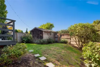 The fully fenced backyard offers a balance of greenery and function, featuring a rustic storage shed and garden beds.