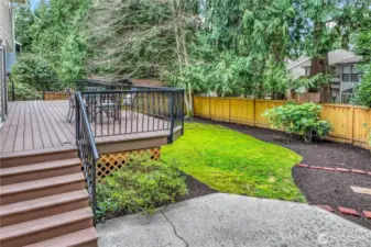 The landscaped yard below the deck features mature trees, shrubs, and a well-maintained lawn, offering space for gardening or outdoor activities. The latticework under the deck adds a polished aesthetic and practical storage potential.