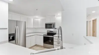 Kitchen features white sleek cabinetry and new stainless steel appliances.