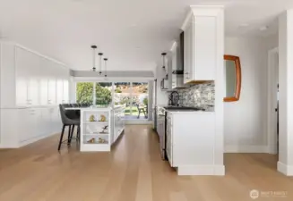 Primary residence kitchen showing bank of pantry cabinets at left, rear patio through the floor to ceiling windows and entrance to the primary suite at right. Not shown is the sliding door to patio is at left of windows.