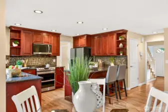 Wide view of the open layout, connecting the kitchen to the adjacent dining nook and main living spaces, with island seating and great sight lines for everyday living and entertaining.