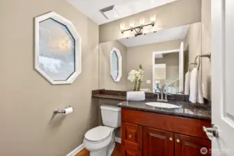 Main floor powder room with granite vanity, oversized mirror, and updated lighting, finished with warm wood flooring. Adds convenience for guests and everyday living.