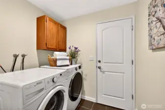 Laundry area located off the garage, with side by side washer and dryer, durable tile flooring, and convenient storage above.