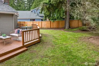 A broader yard view highlights the lawn area and privacy elements, including fencing and established trees. The space feels open enough to enjoy, while still buffered from neighboring homes.