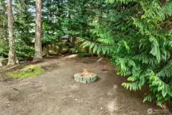 A tucked away fire pit area creates a second outdoor destination, set under a canopy of evergreens. It feels private, quiet, and perfect for evening gatherings. This kind of separate outdoor “room” is a standout feature.