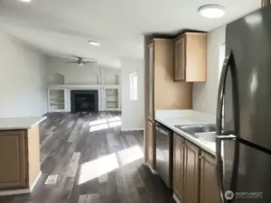 An Opposite View Picture of the Huge Kitchen Showing Ample Cabinet Space, Newer Counter Tops, LED Lighting, All Stainless Appliances Including Built In Microwave, Glass Top Stove Oven, Trim, and Vinyl Plank Flooring Looking into the Second Living Area off the Kitchen And Dining Room.