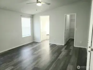 An Opposite View of the Huge Primary Master Bedroom from the Double Entry Doors Showing Newer Trim, and Vinyl Plank Flooring and Looking at the Primary Bath Room and Walk In Closet.