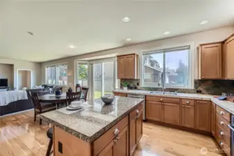 This open-concept kitchen seamlessly flows into the eating space and family room, creating the perfect layout for modern living and entertaining. Natural light pours in through oversized windows and a sliding glass door that leads to the backyard, offering a bright and inviting atmosphere. The spacious kitchen boasts warm wood cabinetry, granite countertops, a central island with bar seating, and a double sink perfectly positioned under a large window with backyard views. Whether you're hosting guests or enjoying a quiet evening at home, this space offers comfort, function, and timeless style.