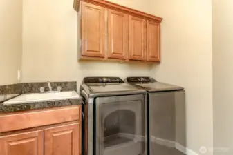 Practical upstairs laundry room with utility sink and storage cabinets
