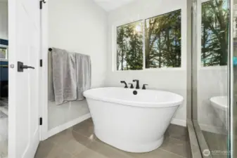 The primary bathroom feels like a private spa, featuring a soaking tub set beneath a sun-filled window with tranquil treetop views. Clean lines, modern fixtures, and serene finishes create a relaxing retreat at the end of the day.