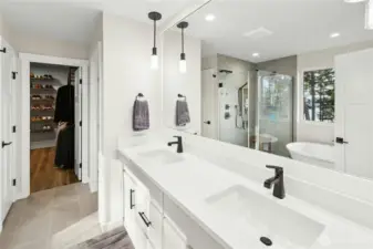 The primary bath features a spacious double vanity with sleek quartz counters, modern fixtures, and ample storage. A glass-enclosed shower and soaking tub complete this bright, spa-like retreat designed for comfort and style.