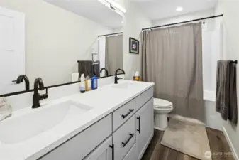 The shared upstairs bathroom features a modern double vanity with quartz countertops and contemporary fixtures. Designed for convenience, it comfortably serves the three additional bedrooms with ample space and storage.