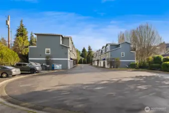 View of the community looking from the unit. Ample guest parking and communal trash bin on the left.