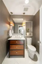 The powder room with stone flooring features a lovely vanity, art niche and decorative wallpaper & accents