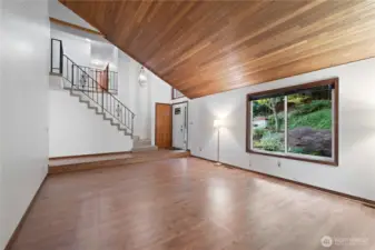 Living room with laminate flooring, cedar vaulted ceiling, built in bookcases and a wood burning fireplace