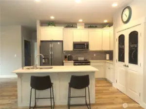 THE GREAT ROOM INCLUDES THIS GORGEOUS BRIGHT KITCHEN WITH SLAB COUNTER TOPS, WHITE CABINETRY, BLACK APPLIANCES, PLUS DOUBLE DOOR PANTRY!