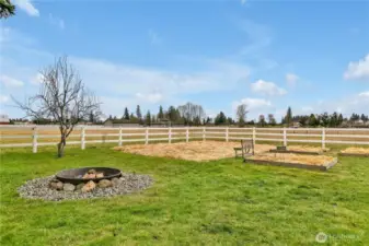 Back yard with fire pit, garden space and fruit trees looking out toward the hay field