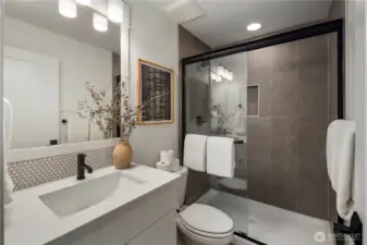 Lower-Level Bathroom: Sleek full bathroom with modern finishes, a frameless glass shower, and designer tile accents. Perfectly situated to serve the lower-level suite or bonus space, it adds functionality and privacy for everyday living or overnight guests.    Photos are from the model home at Foxmoore and for visualization purposes only. Plans, colors, building orientation, finishes, home outlook, and other details can and WILL vary.